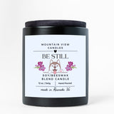 Candle with 'Be Still' label featuring a dog illustration on a white background