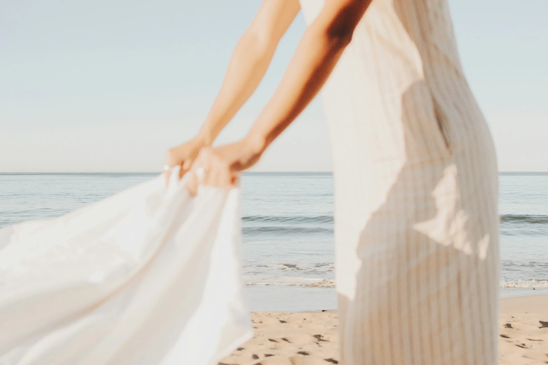 Person in a flowing dress on a beach with ocean view