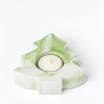 Green and white tree-shaped candle holder with a lit candle on a white background