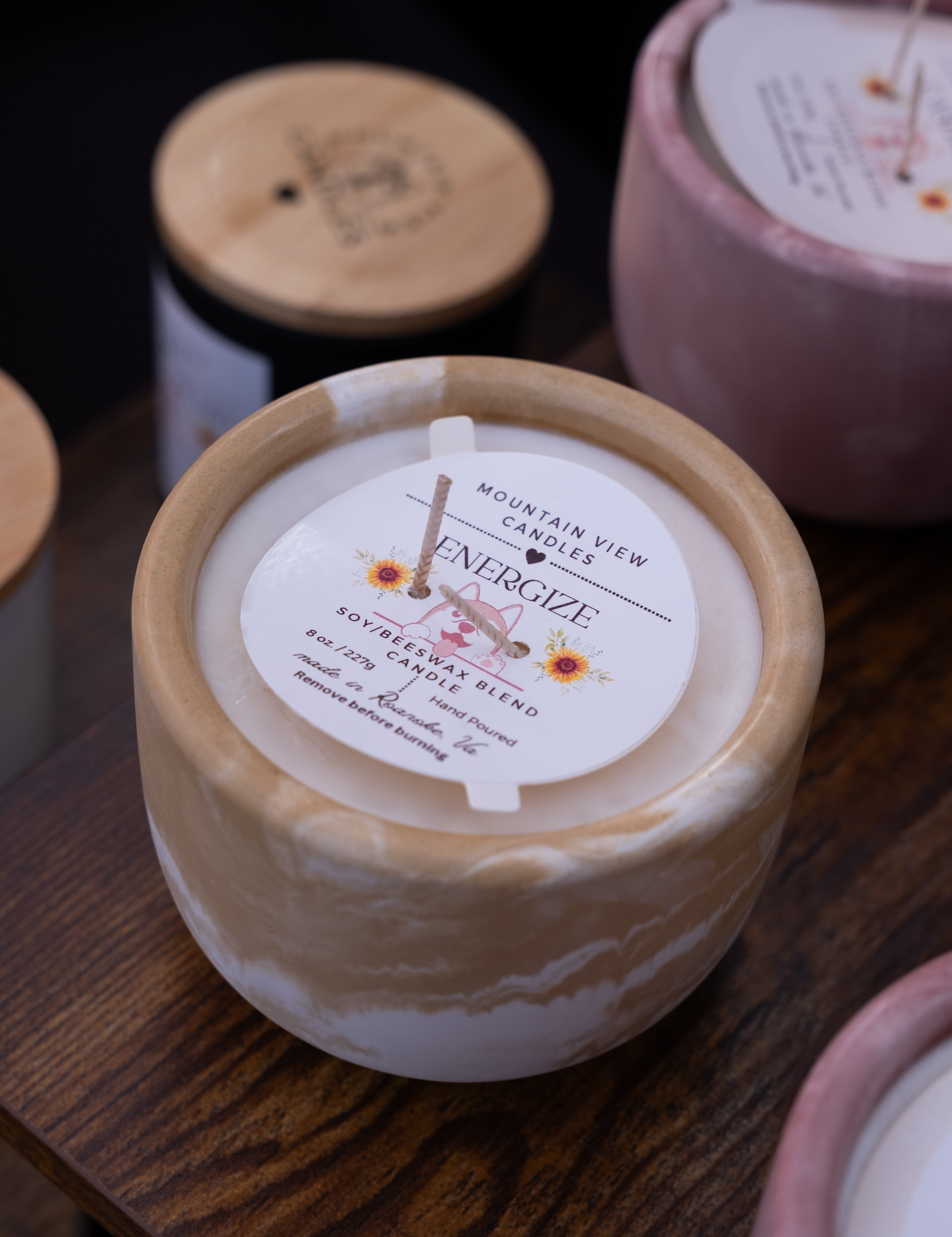 Candle with a label on a wooden surface, surrounded by other candles.