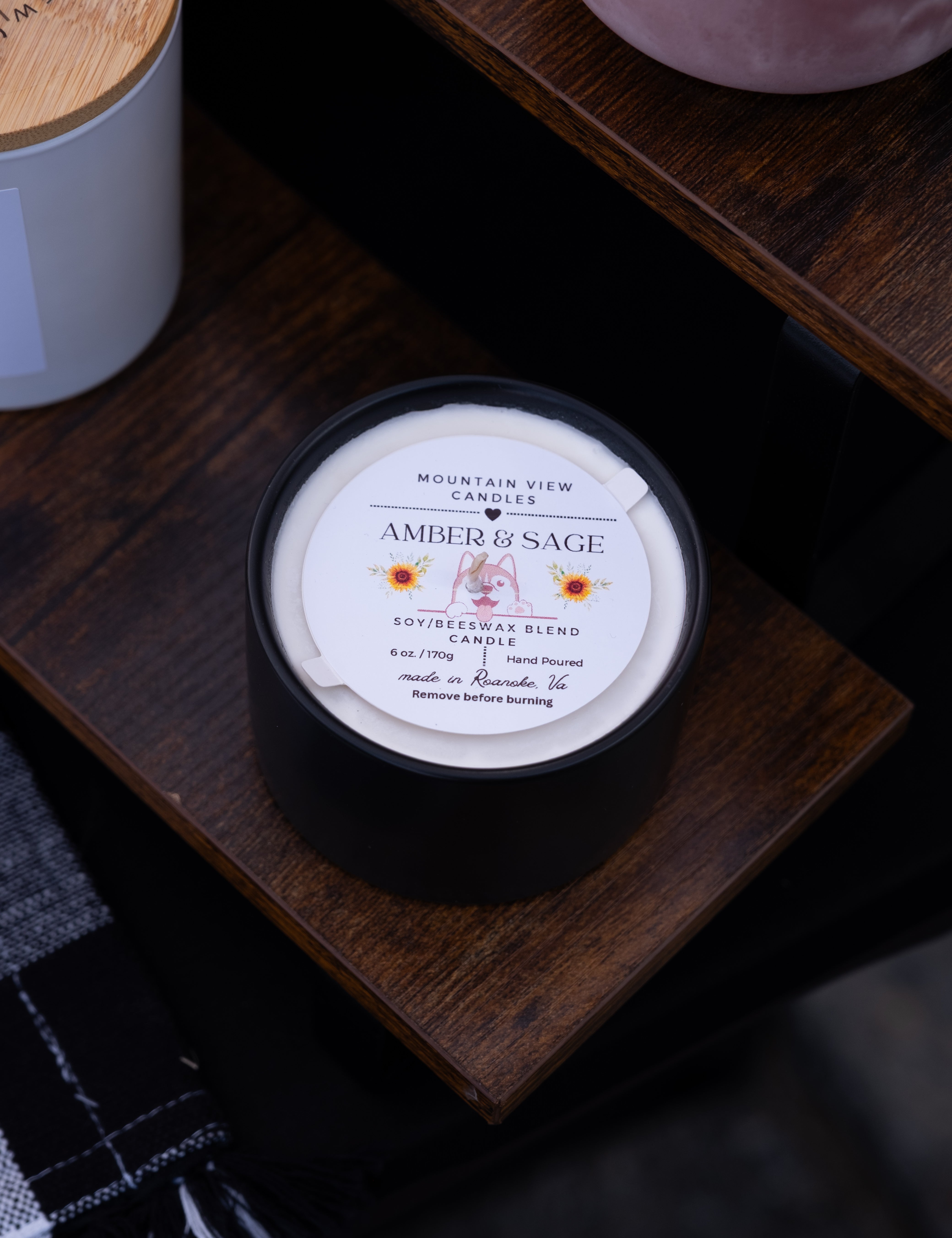 Candle labeled 'Amber & Sage' on a wooden surface with a blurred background