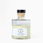 Clear glass bottle with wooden cap labeled 'Linens' on a white background