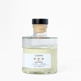 Clear glass bottle with wooden cap labeled 'Linens' on a white background