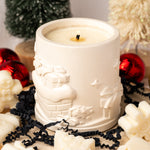 White candle in a decorative holder surrounded by Christmas ornaments on a light background