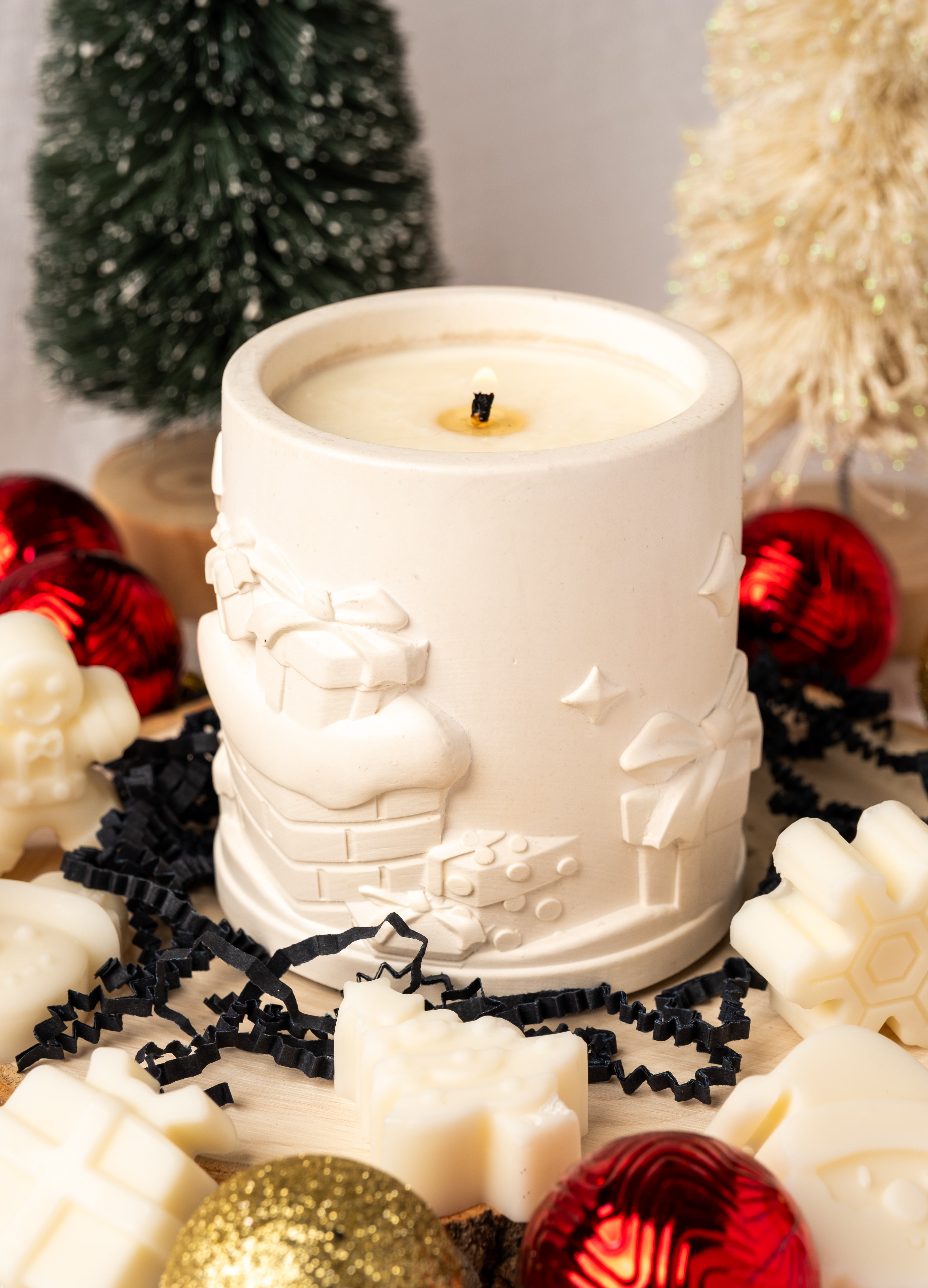 White candle in a decorative holder surrounded by Christmas ornaments on a light background