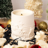 White candle with decorative design surrounded by Christmas ornaments and decorations.