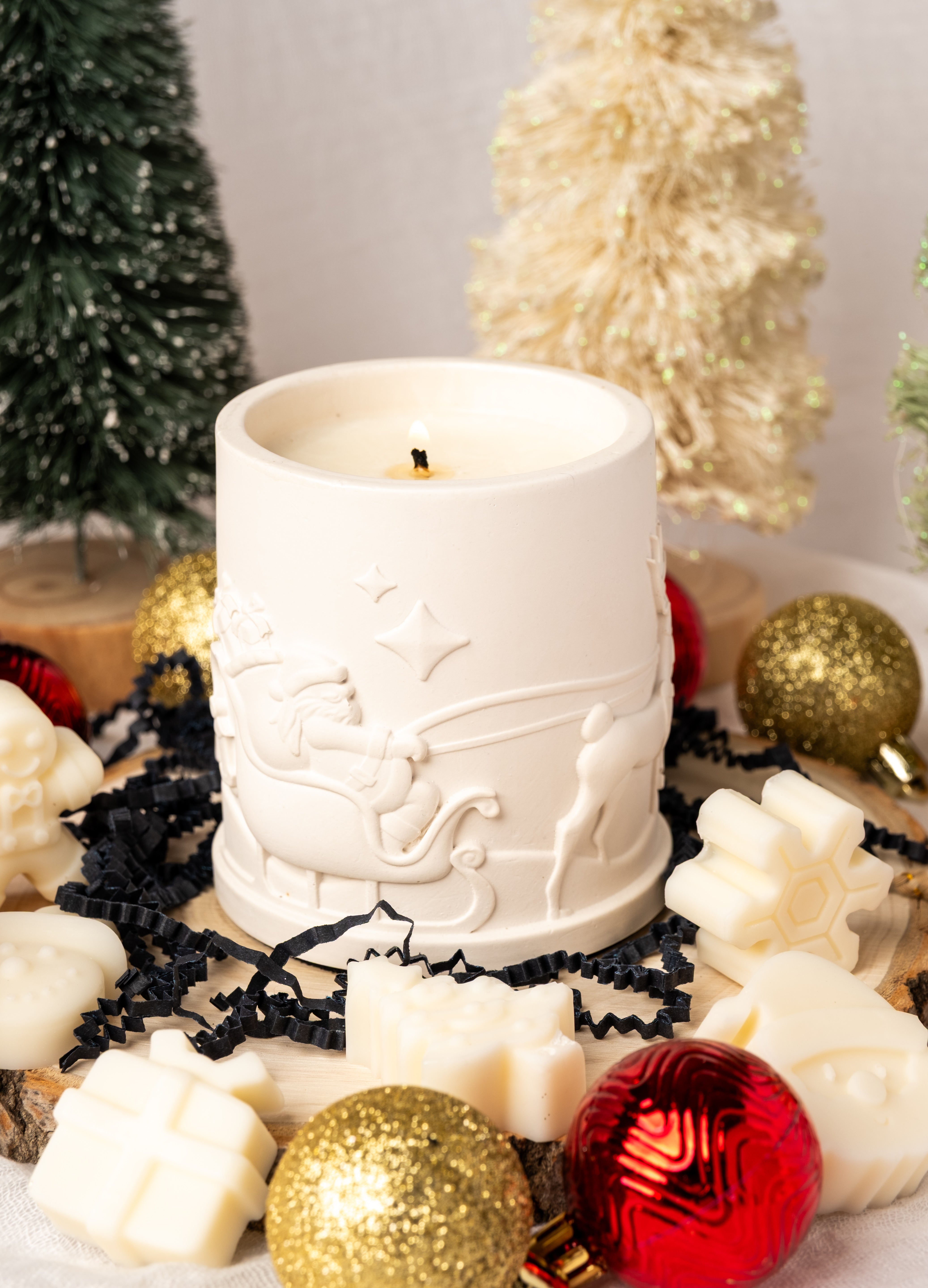 White candle with decorative design surrounded by Christmas ornaments and decorations.