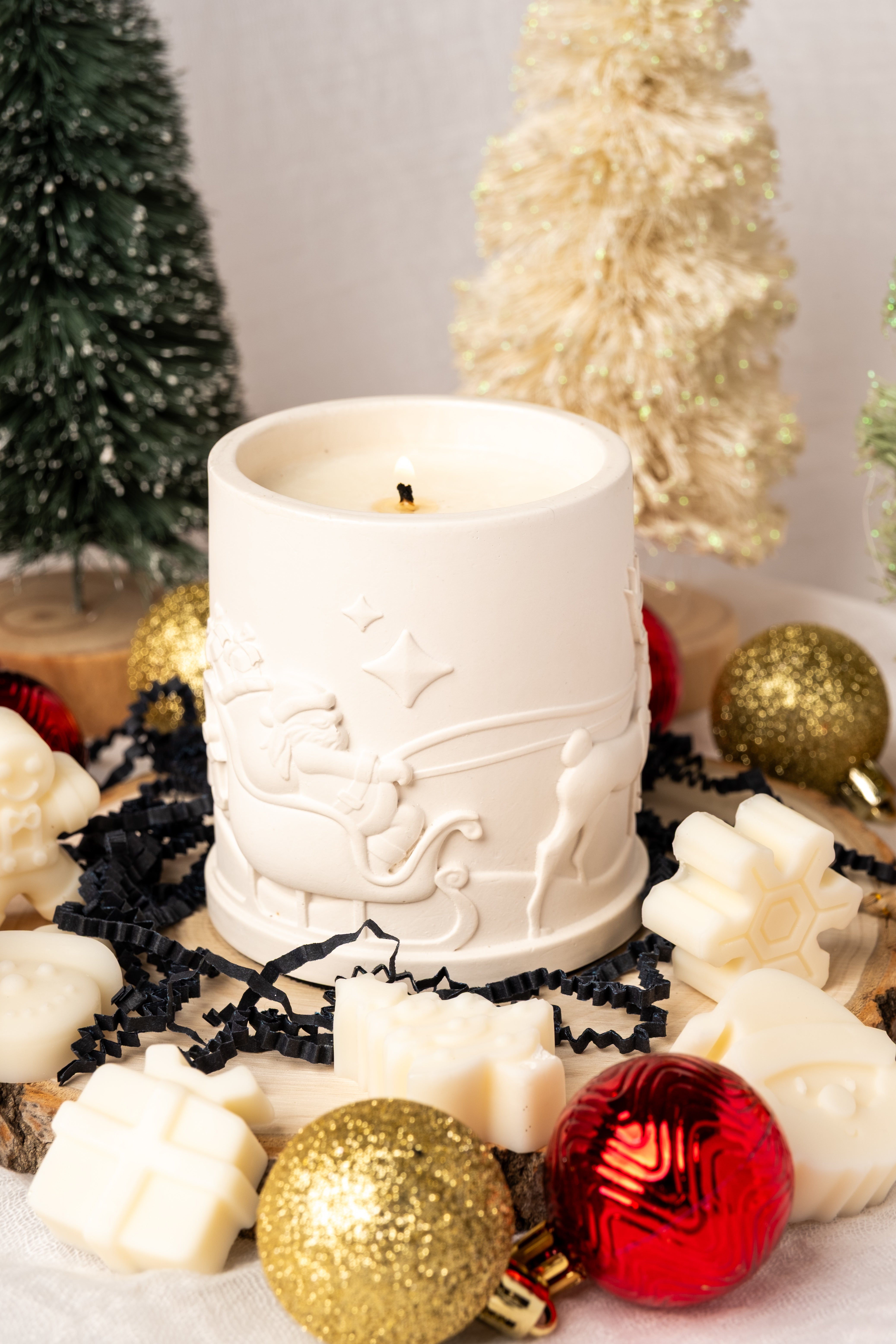 White candle with decorative design surrounded by Christmas ornaments and decorations.