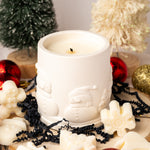 White candle with Santa Claus design surrounded by Christmas decorations on a light background