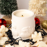 White candle with Santa Claus design surrounded by Christmas decorations on a light background