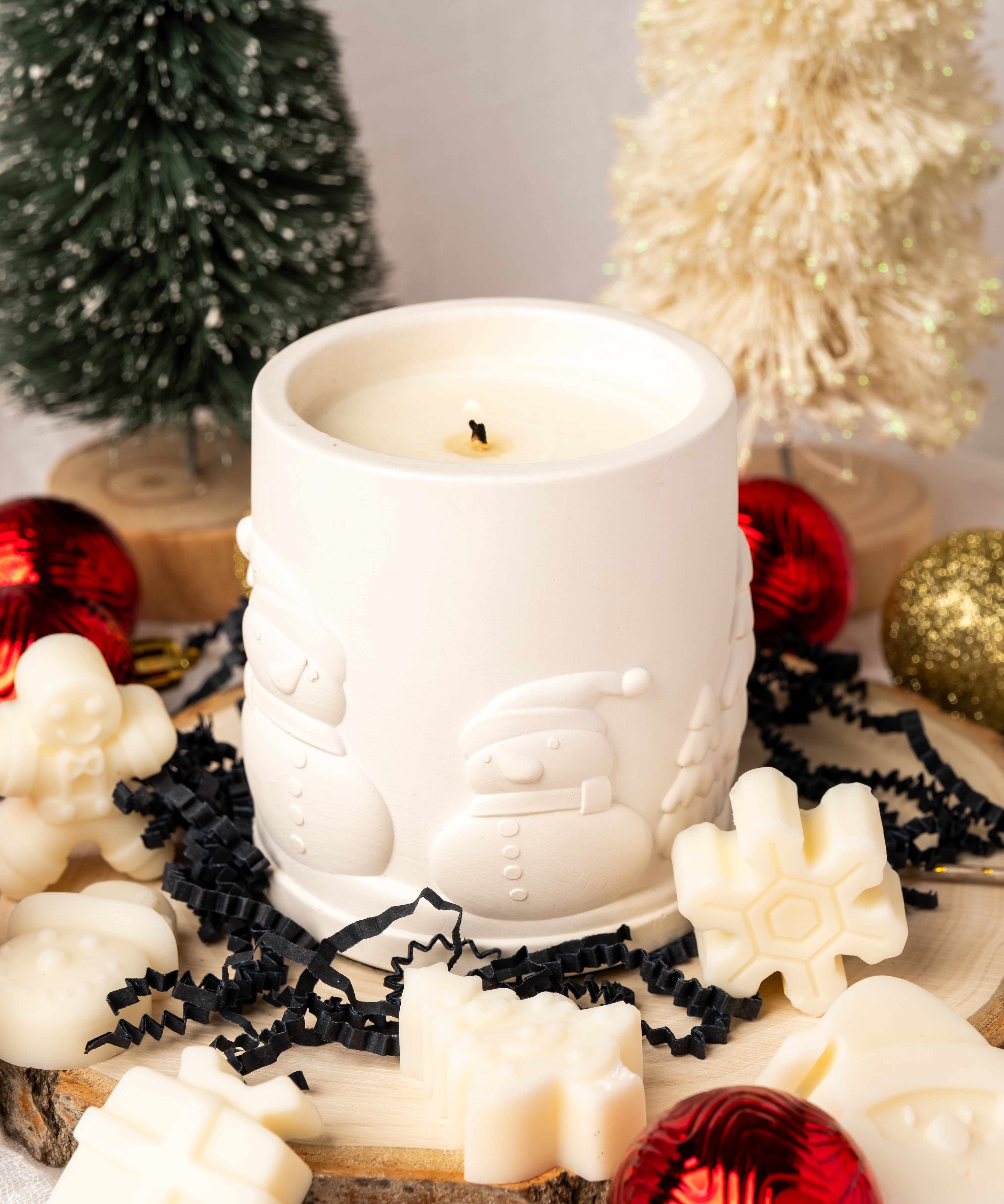 White candle with Santa Claus design surrounded by Christmas decorations on a light background