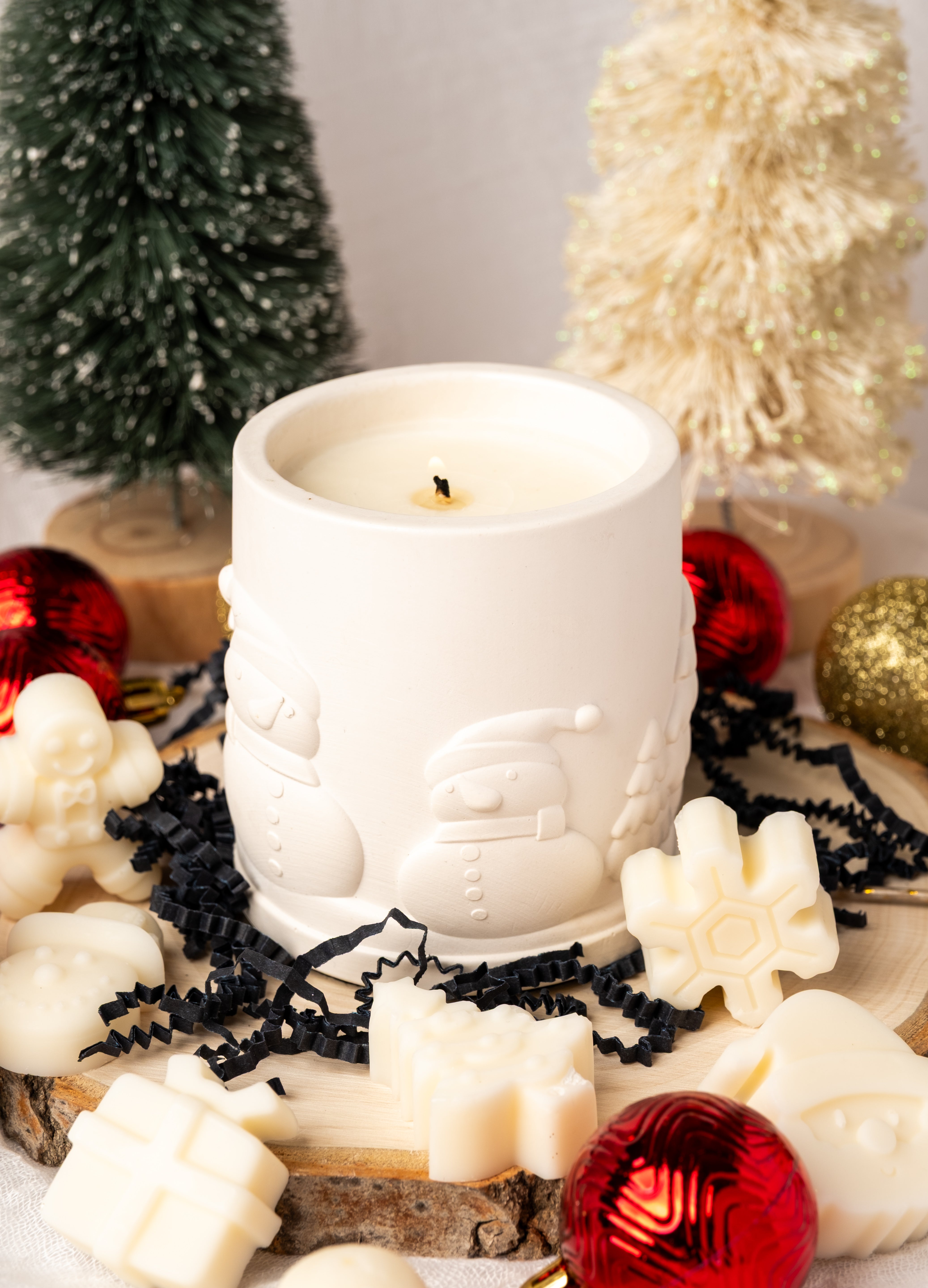 White candle with Santa Claus design surrounded by Christmas decorations on a light background