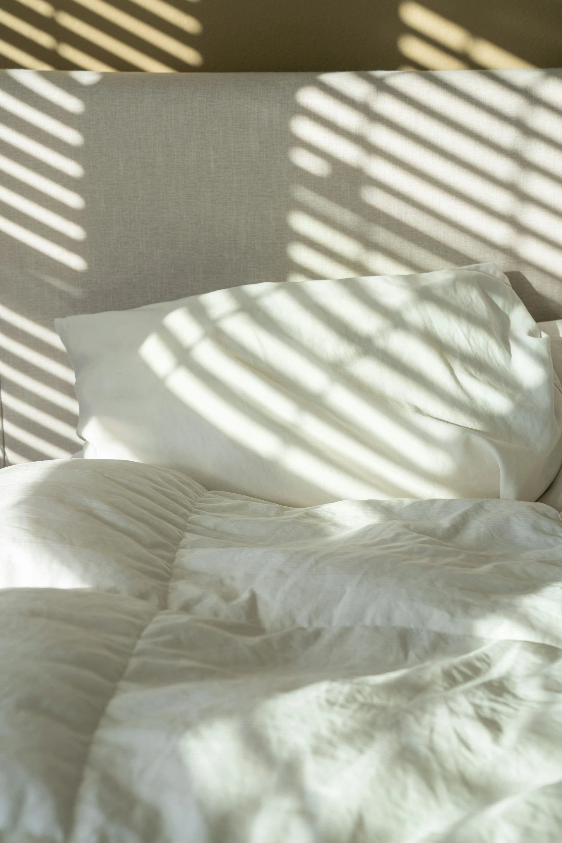 White bedding with shadows from window blinds on a bed