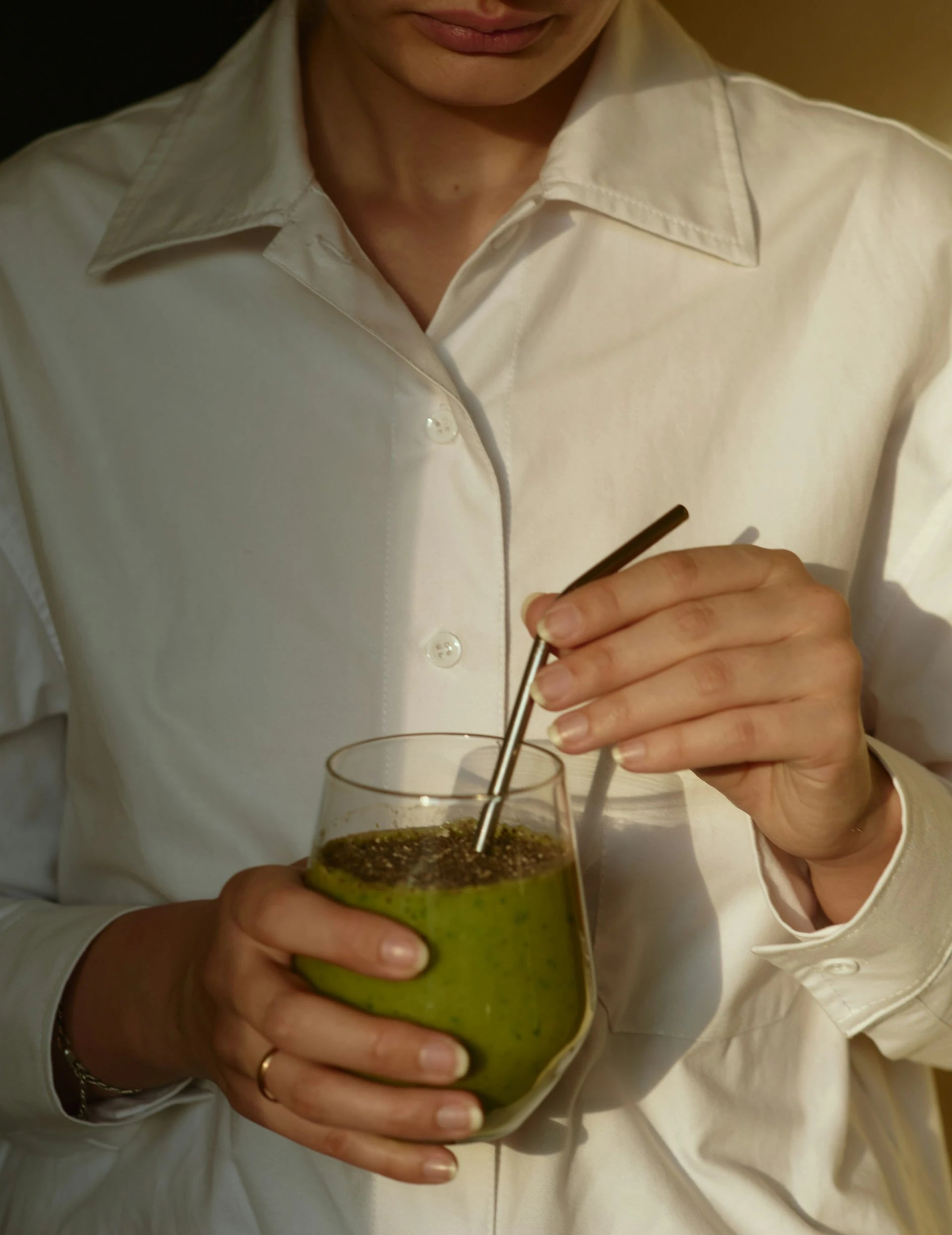 Person holding a green smoothie with a straw, wearing a white shirt.